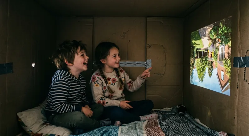 Camera Obscura aus einem großen Transportkarton, in dem 2 Kinder Platz haben. Bild erstellt mit KI